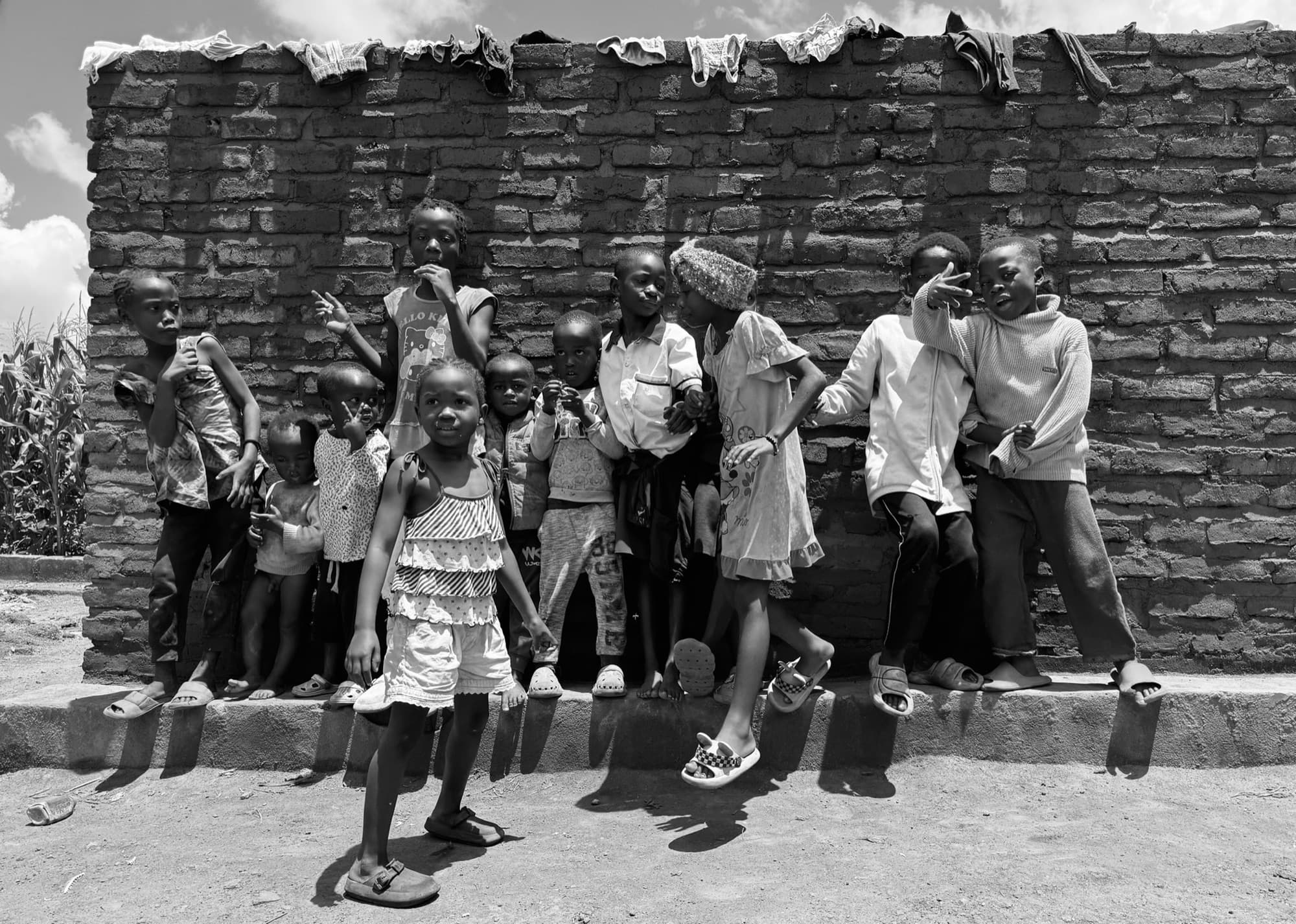 Crianças do Malawi posando em frente a um muro de tijolos com roupas no varal