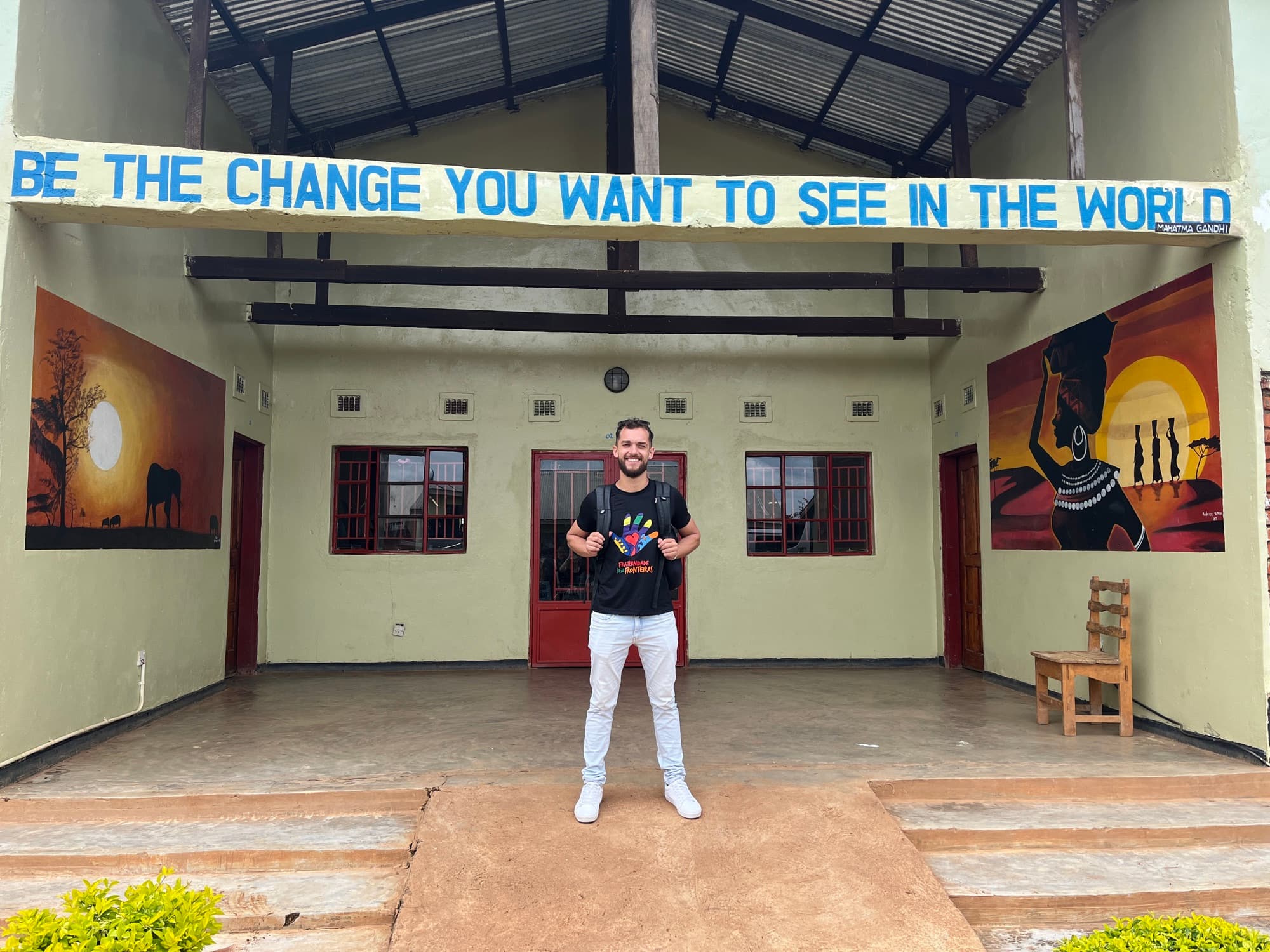 Felipe em frente à escola da Fraternidade sem Fronteiras, sob a frase de Gandhi: Be the change you want to see in the world